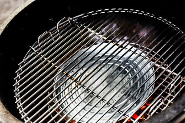 Big Green Egg grill belseje rozsdamentes ráccsal és alatta elhelyezett, gőzölgő alumínium csepegtető tálcával indirekt grillezéshez

