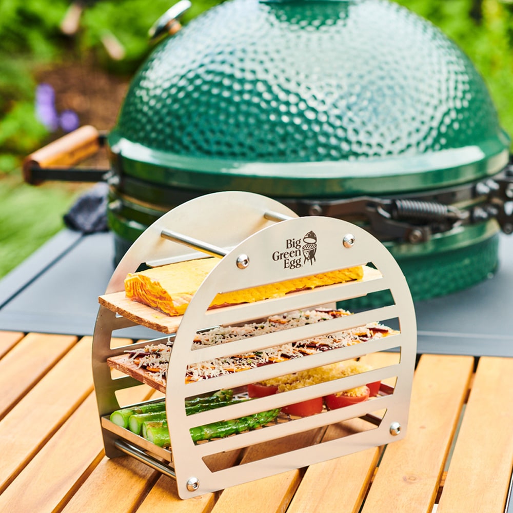 Big Green Egg füstölő torony feltöltve zöldségekkel, sajttal és hallal, kültéren elhelyezve grill mellett

