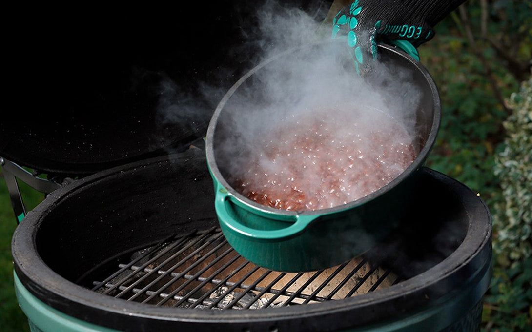 Gőzölgő étel Big Green Egg kerek öntöttvas lábasban grillezés közben, kültéri használatban.