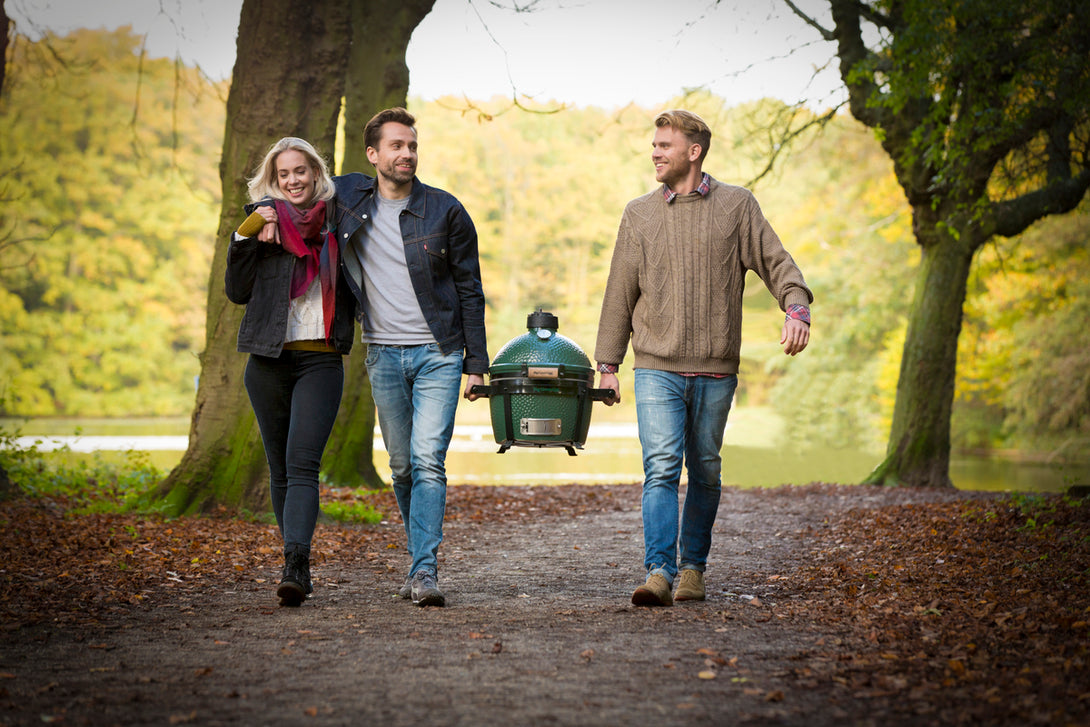 Három fiatal sétál az erdőben, közösen visznek egy MiniMax Big Green Egg grillt – mobil grillezés hangulatkép