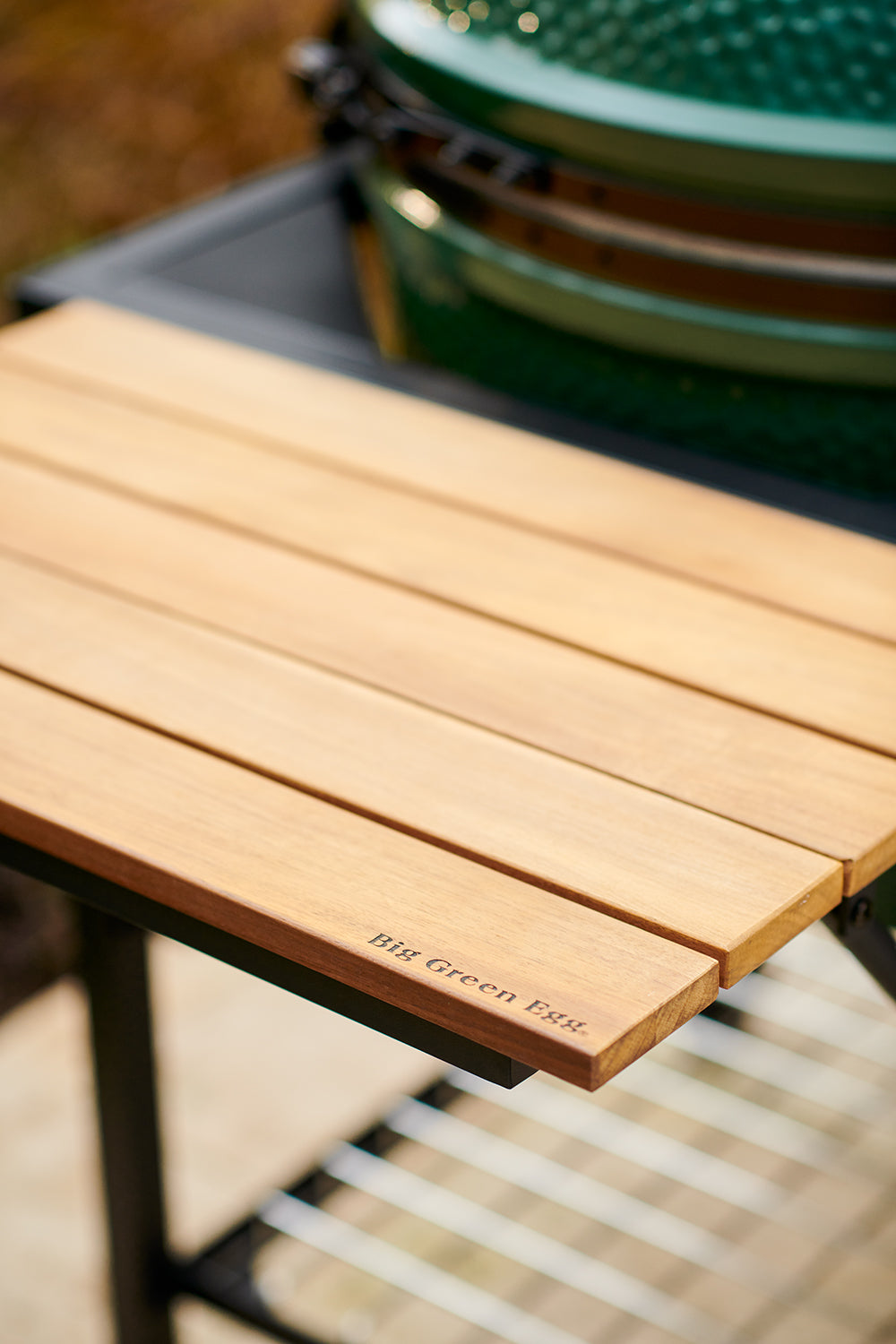 Közelkép teakfa lehajtható polcról Big Green Egg logóval, kültéri grillasztalon
