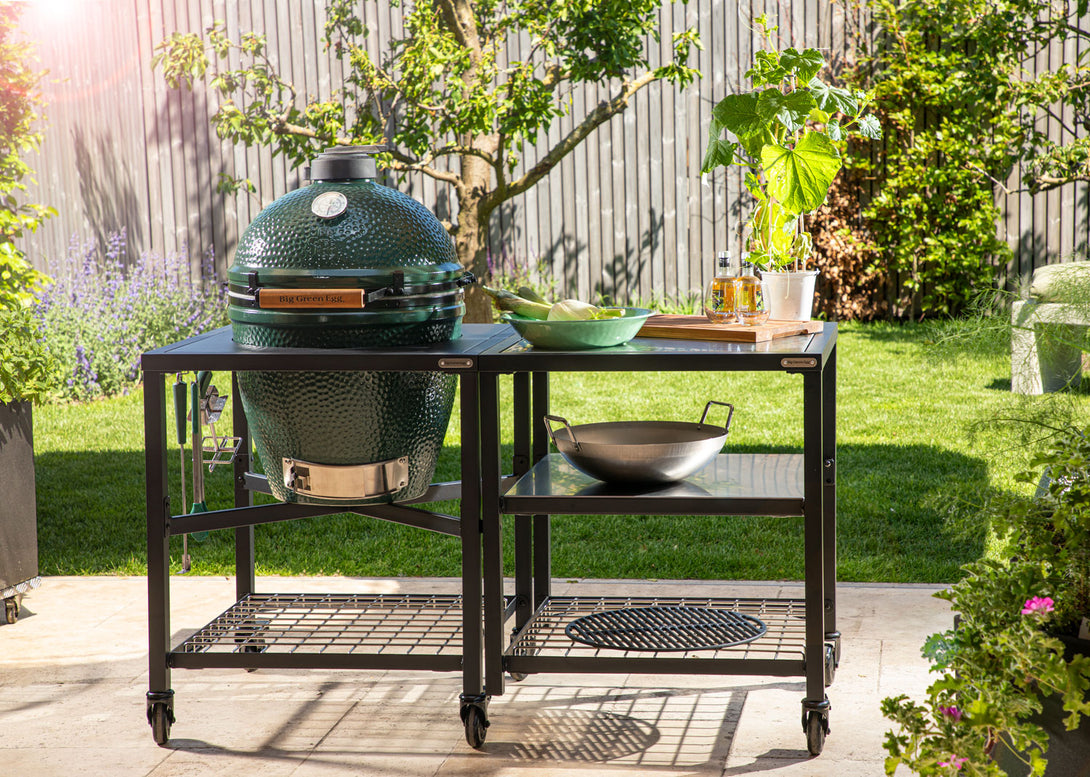 Big Green Egg kültéri grillrendszer rozsdamentes rácspolcokkal és grillező kiegészítőkkel napfényes kertben