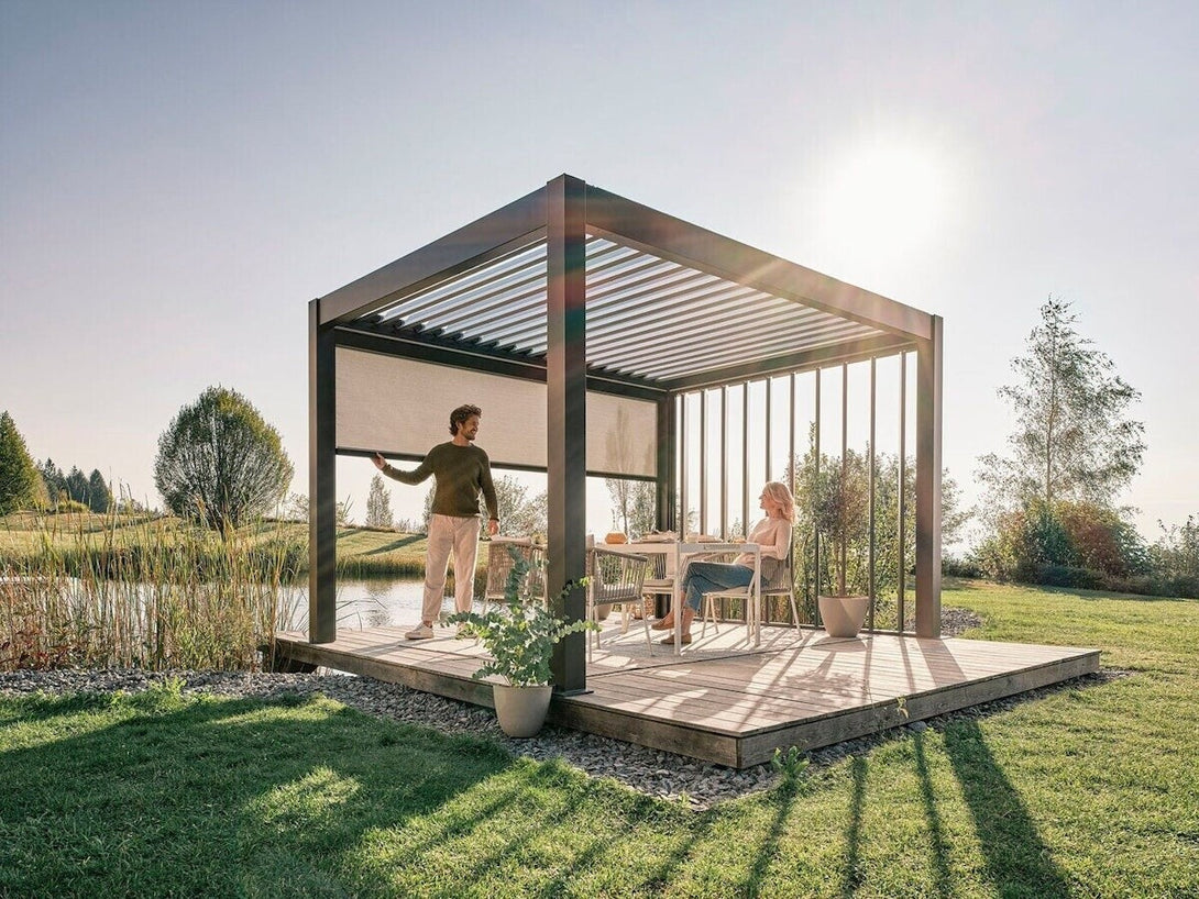 Biohort pergola sötétszürke-metál színben, tóparti stégen, lehúzható árnyékolóval felszerelve, két emberrel a kerti étkezőrészen napsütéses környezetben.
