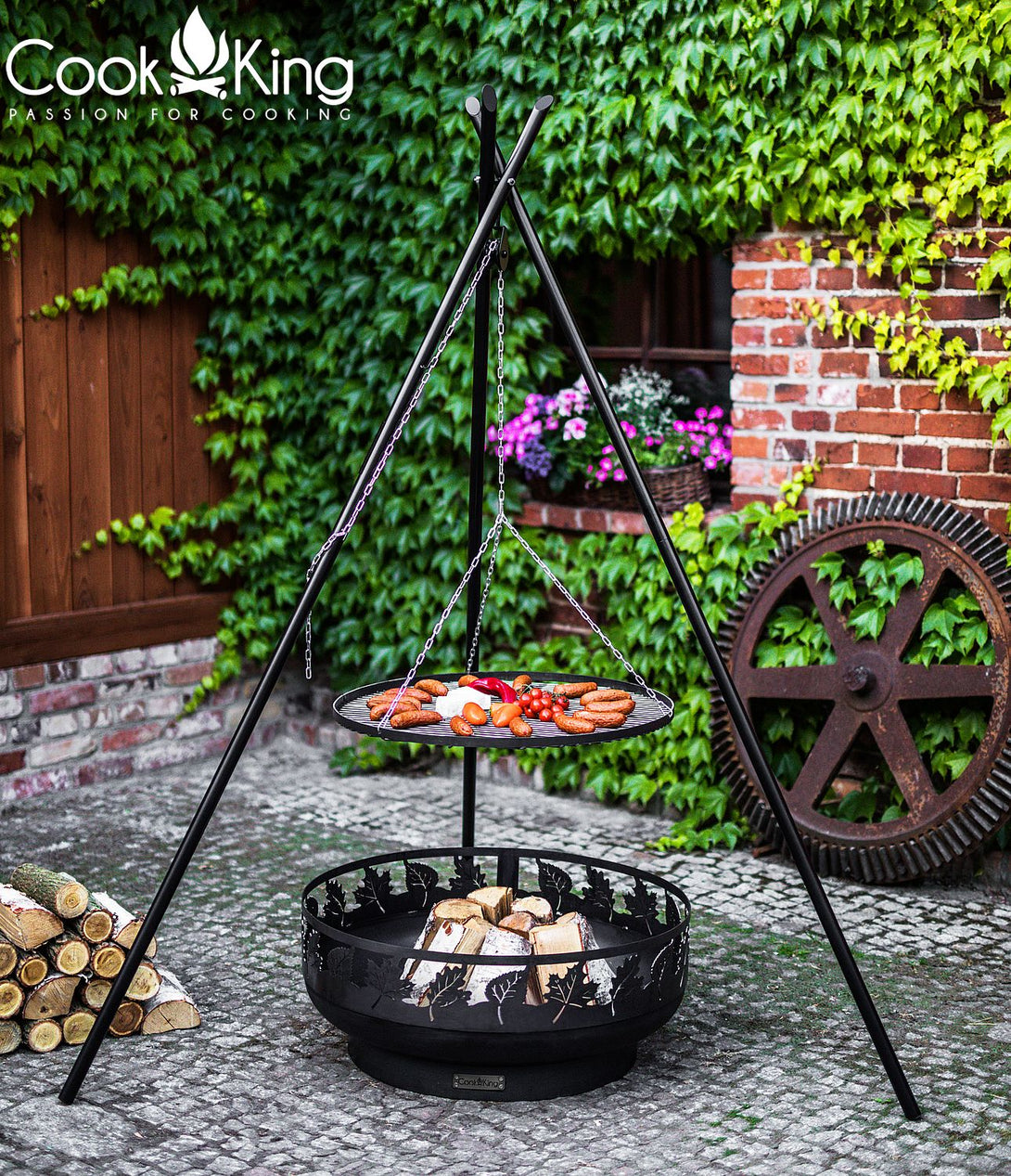 Háromlábú állványos grill kerti tűzrakó felett, nagy függesztett ráccsal és ételekkel, kültéri használat.