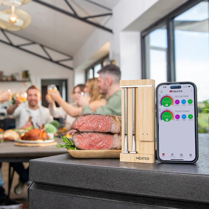 MEATER vezeték nélküli húshőmérő szaftos steak és mobilalkalmazás mellett, baráti vacsora háttérben