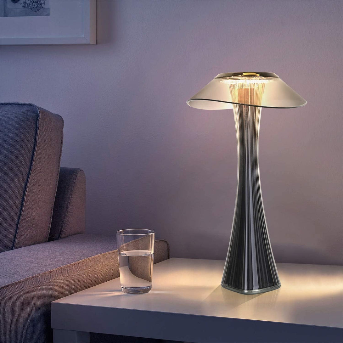 Világító LED asztali lámpa modern nappaliban, fehér dohányzóasztalon pohár és kanapé mellett.