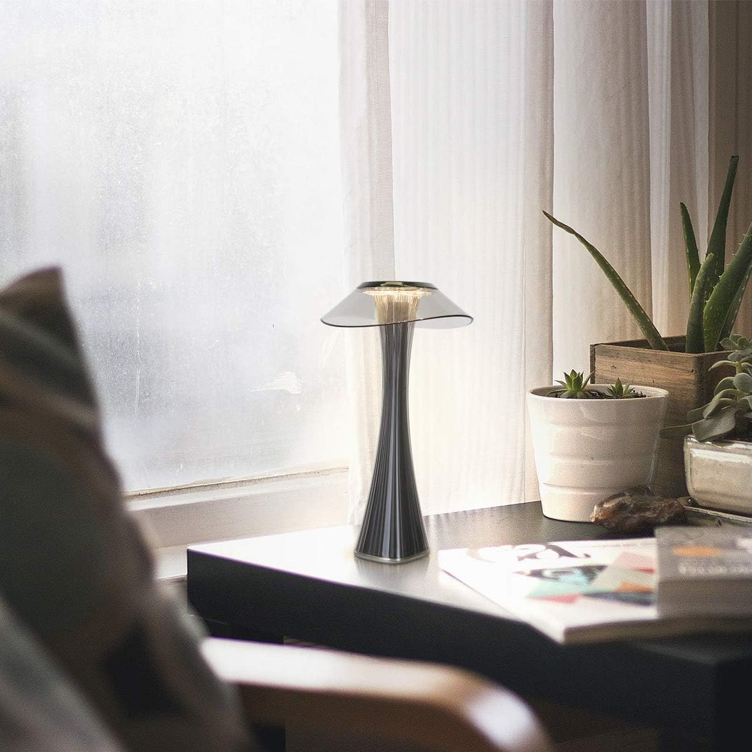 Fekete LED asztali lámpa modern nappaliban, növényekkel és magazinokkal díszített ablakpárkányon.