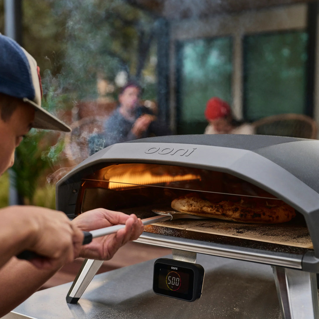 Pizza kivétele az Ooni Koda 2 Pro kemencéből kültéri környezetben, füsttel a háttérben